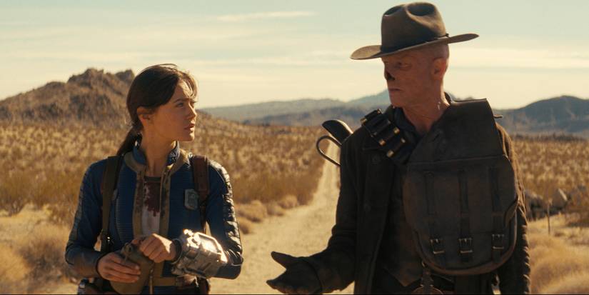 Ella Purnell and Walton Goggins look at each other while walking on a desert road in Fallout Season 2, Episode 4
