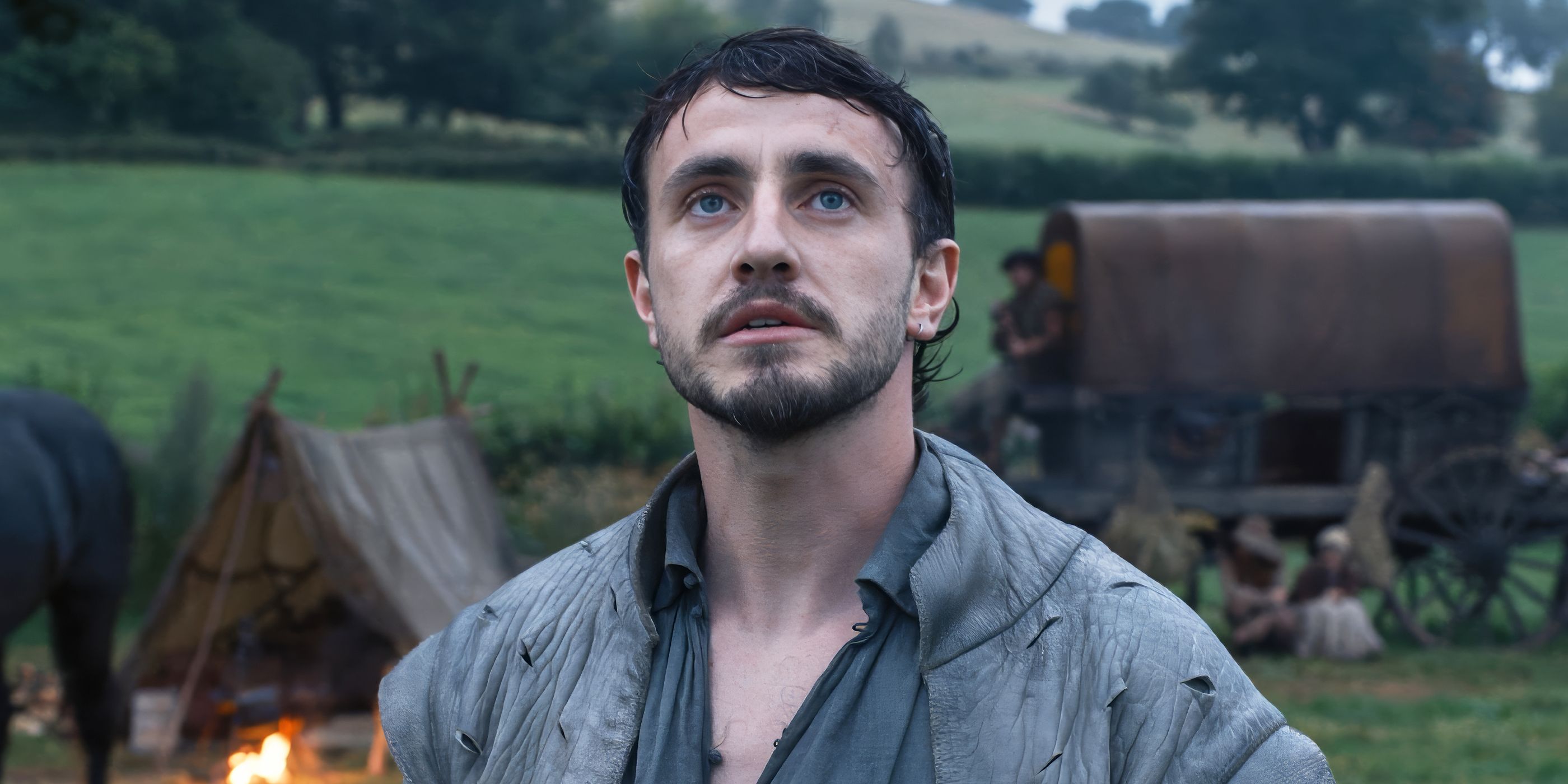 Will stands outside in front of tents and a tented wagon, looking up.