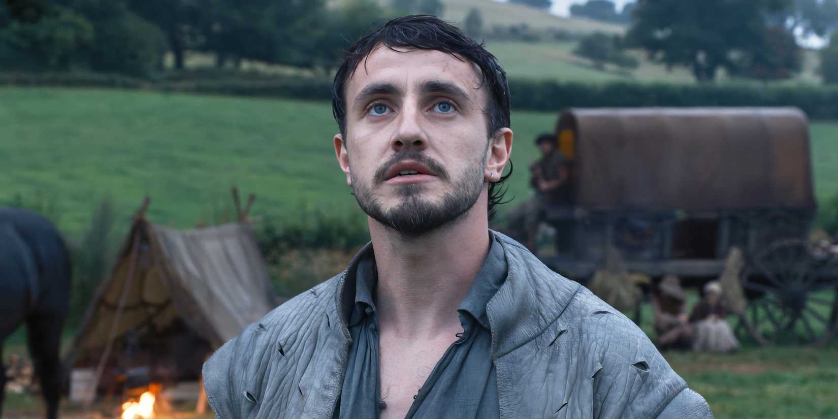 Will stands outside in front of tents and a tented wagon, looking up.