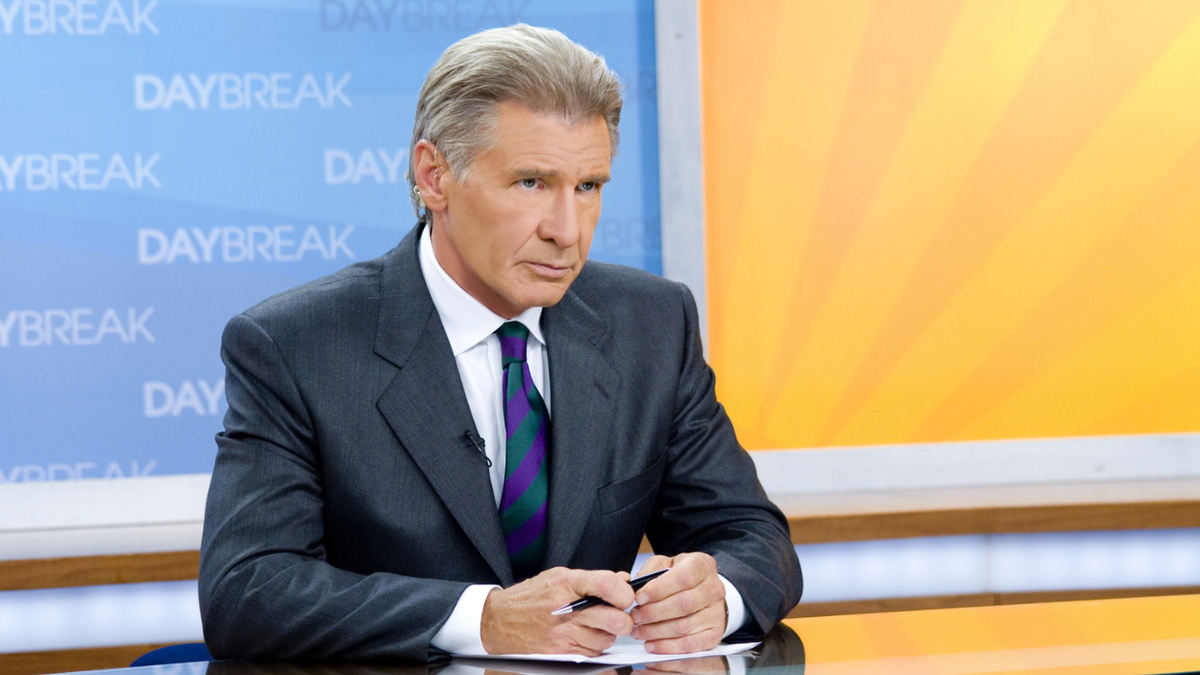 Harrison Ford as Mike in a suit and tie sitting behind a news desk in Morning Glory.