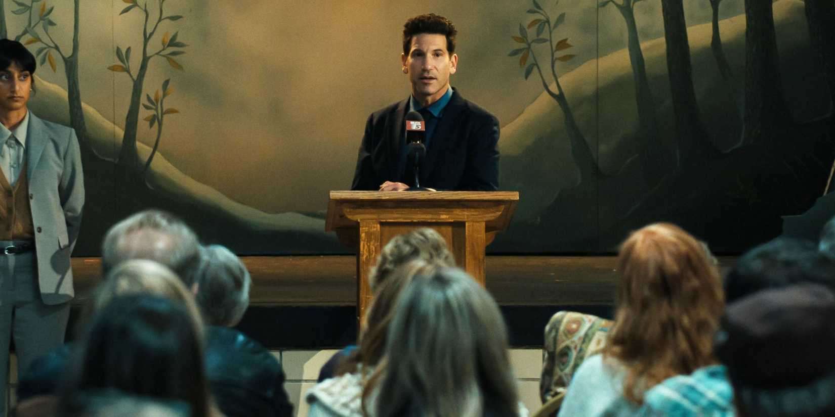 Jon Bernthal's Jack standing at a podium in His & Hers.