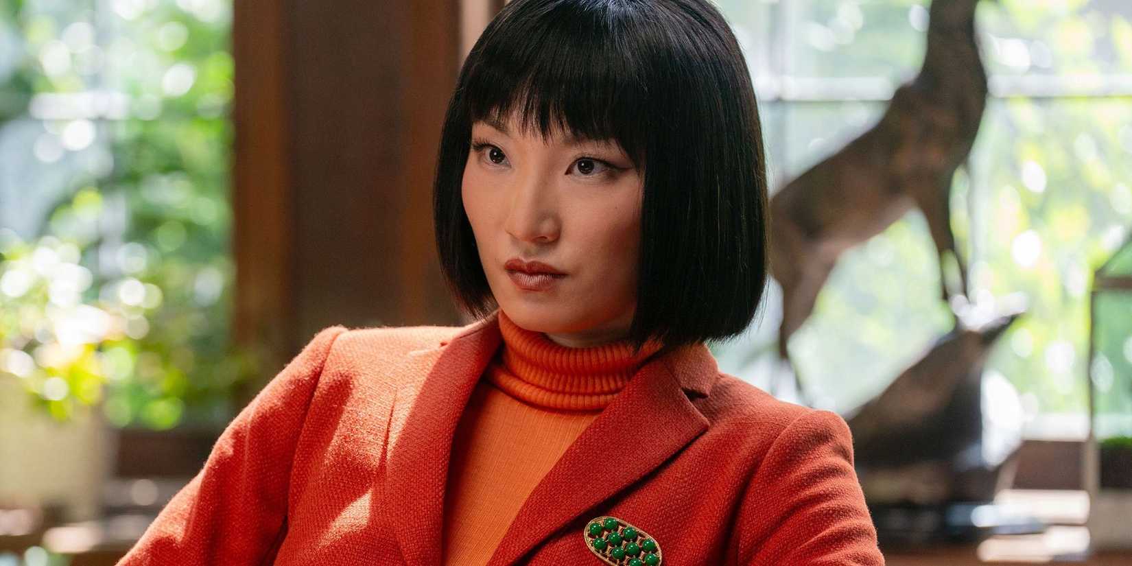 Poppy Liu's Helen wearing an orange turtleneck and orange jacket staring ahead in His & Hers.