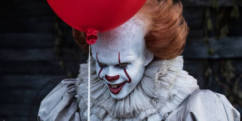 It/Pennywise smiling sinisterly behind a red balloon in the 2017 adaptation of It