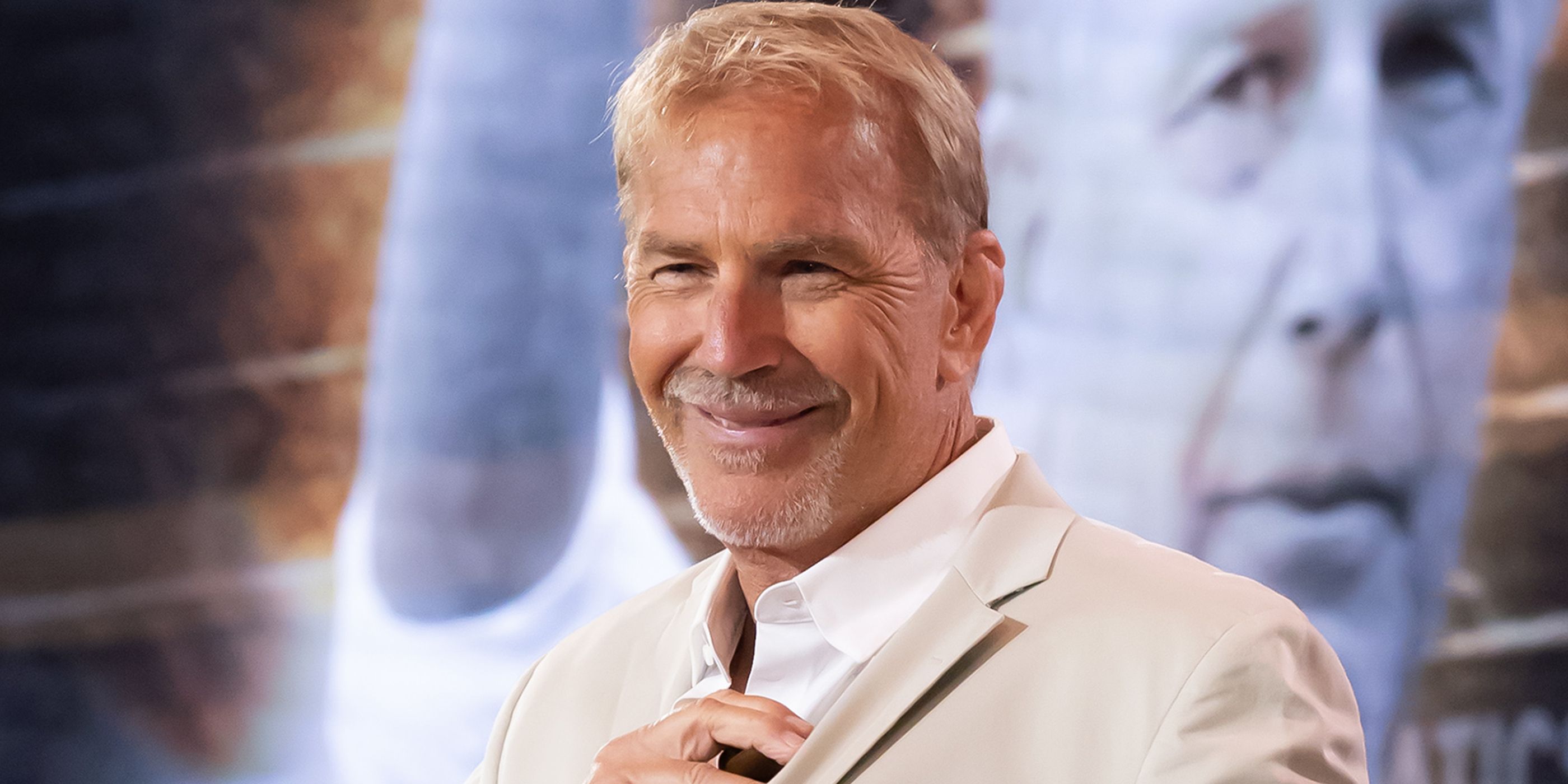 Kevin Costner on the red carpet with an image of a man behind him.