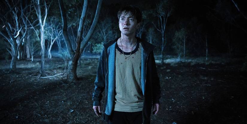 A boy standing in the woods at night.