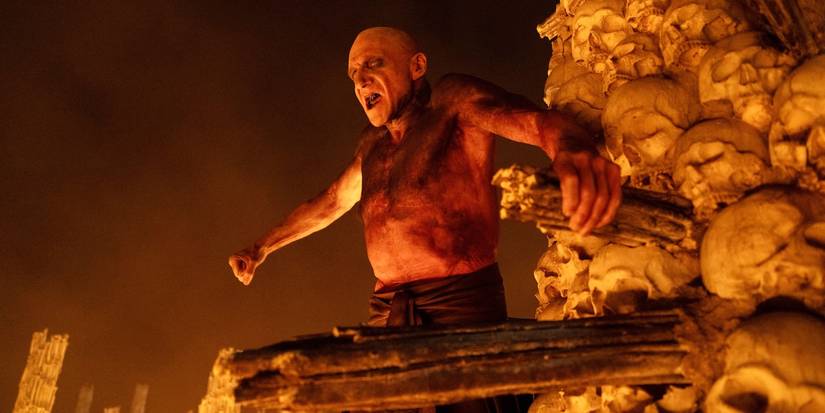 Ralph Fiennes atop a pile of skulls, puffing out his chest, in 28 Years Later: The Bone Temple