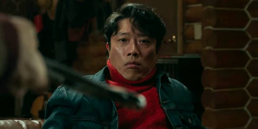A scared man looking at another man's weapon in No Other Choice