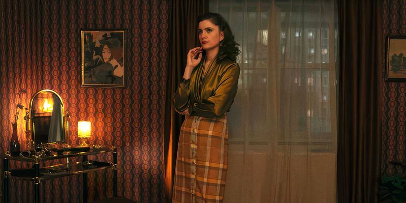 Vic Michaelis as Cheryl standing in her living room in front of the curtain in Ponies