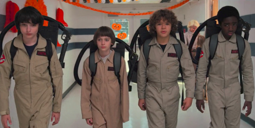 The kids dressed as Ghostbusters walk down a school hallway in Stranger Things.