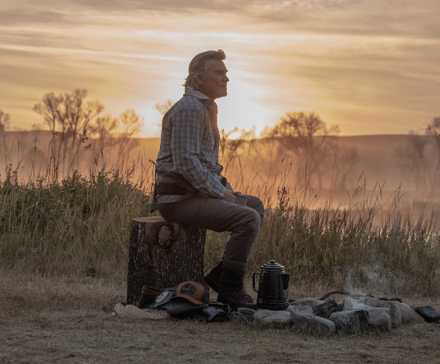 Kurt Russell as Preston Clyburn sitting beside a campfire on 'The Madison'