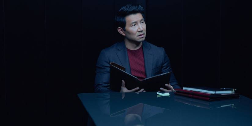 Simu Liu sits at a table reading a file on 'The Copenhagen Test.'