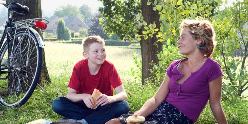 Thomas Doret and Cécile de France sitting on the grass and smiling at each other in The Kid With the Bike.