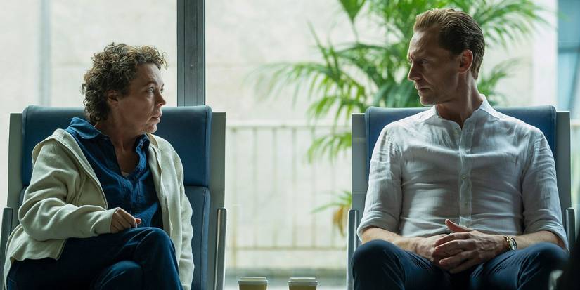 Angela Burr and Jonathaqn Pine sitting side by side and talking in The Night Manager Season 2 Episode 4