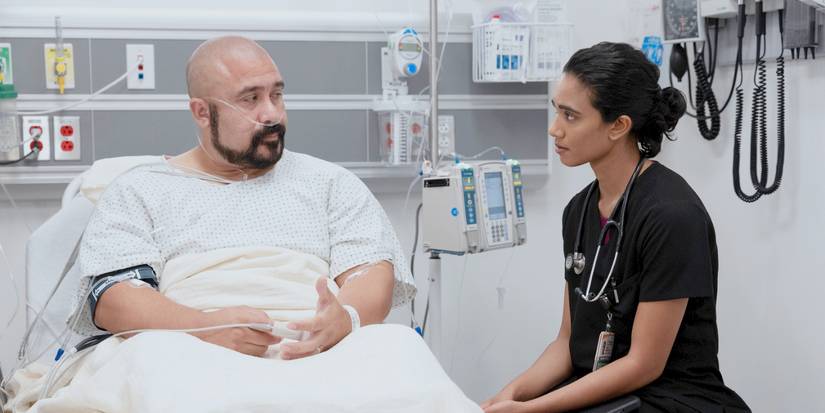 Mohan sitting at Orlando Diaz's bedside as the two talk in The Pitt Season 2 Episode 4