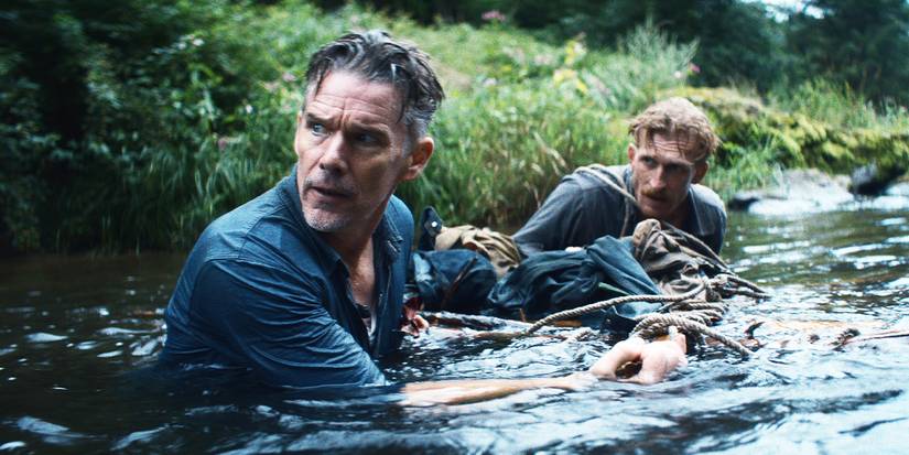 Two men wading through a river, carrying something between them.