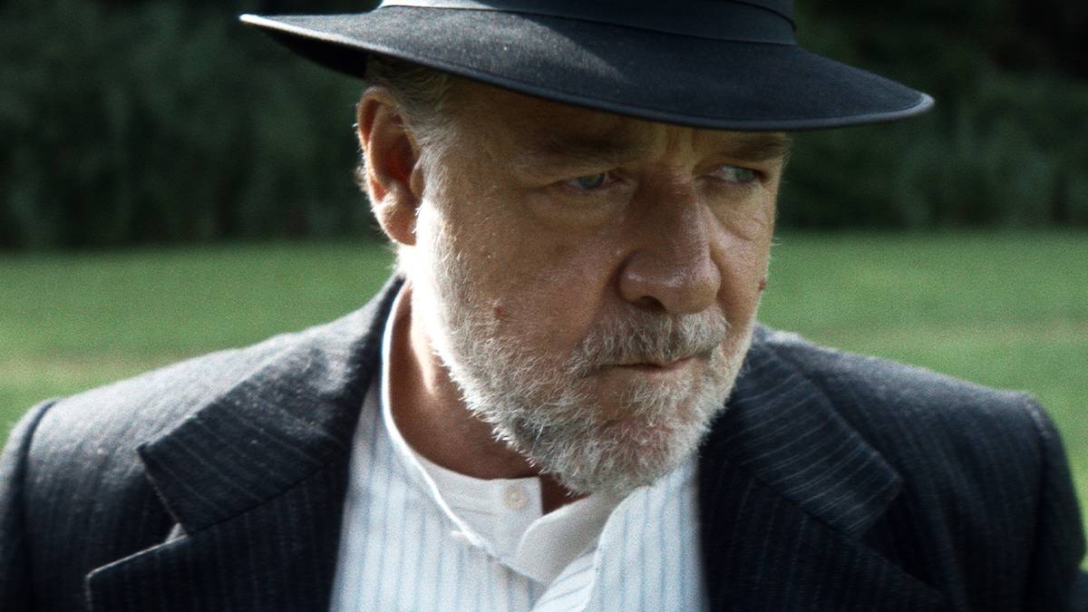 Russell Crowe wears a hat and suit, looking off-camera pensively in The Weight