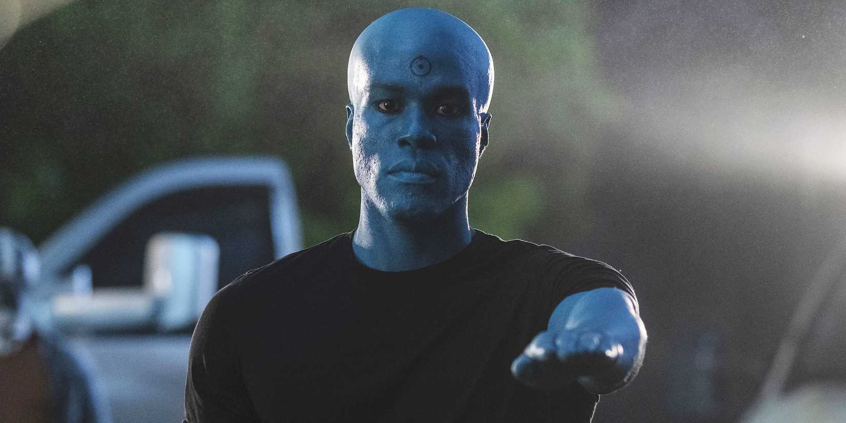 Yahya Abdul-Mateen II sebagai Dokter Manhattan menunjuk lurus ke depan dengan tangan di Watchmen