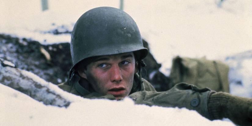 Soldier wearing a helmet peers from a snowy trench, looking tired and alert in A Midnight Clear 1992