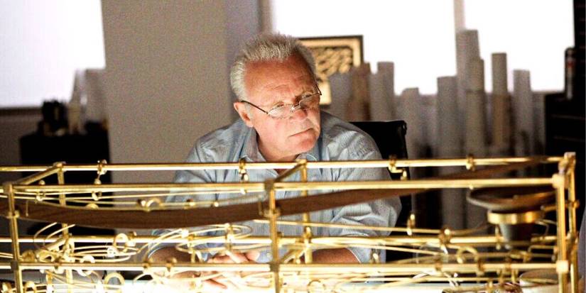 Anthony Hopkins sitting alone at a desk in front of a golden structure in Fracture