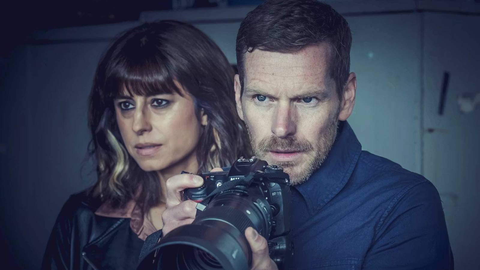 A man looks through a long lens camera next to a woman in 'Betrayal'