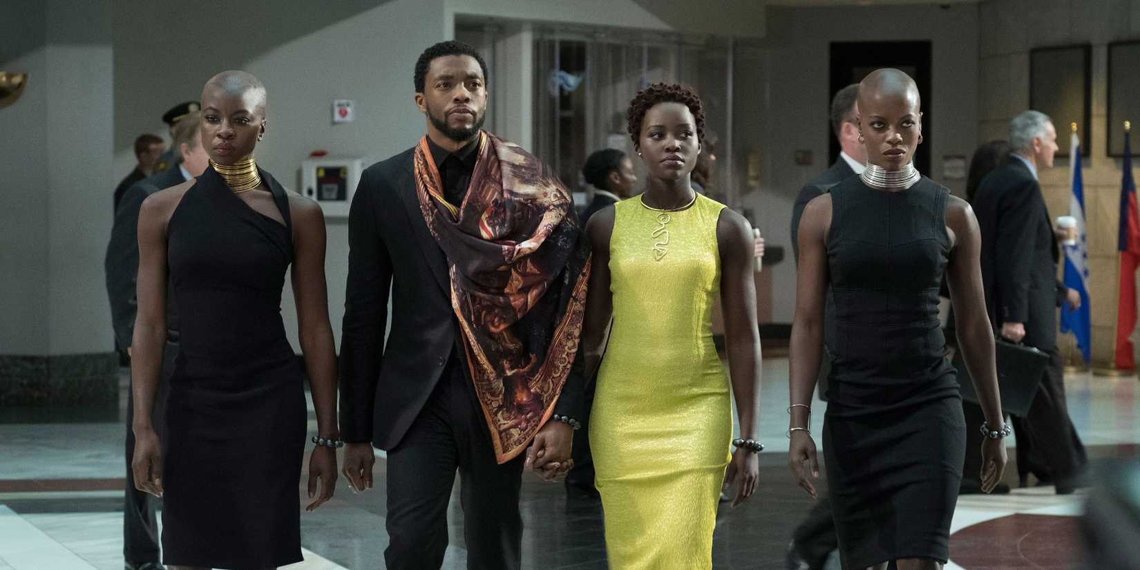 The cast in nice outfits walk intently through an office with purposeful expressions in Black Panther.