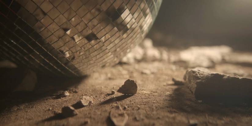 A broken glitterball sits on a dirty concrete floor in promotional image for Murder in Glitterball City.