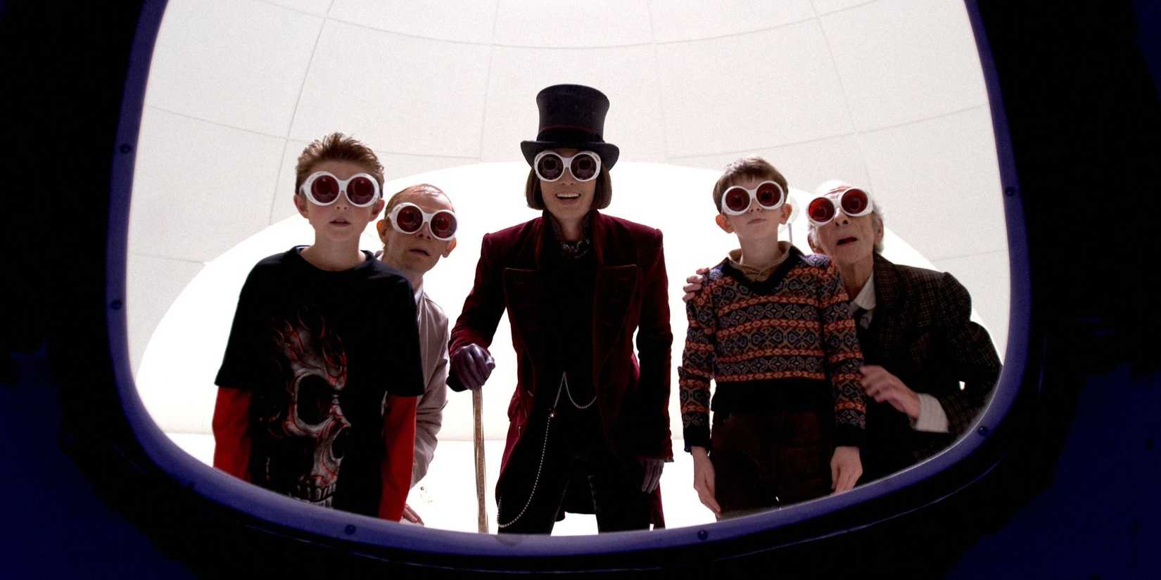 Willy Wonka and a group of kids and adults wear large goggles and look at a screen in Charlie and the Chocolate Factory
