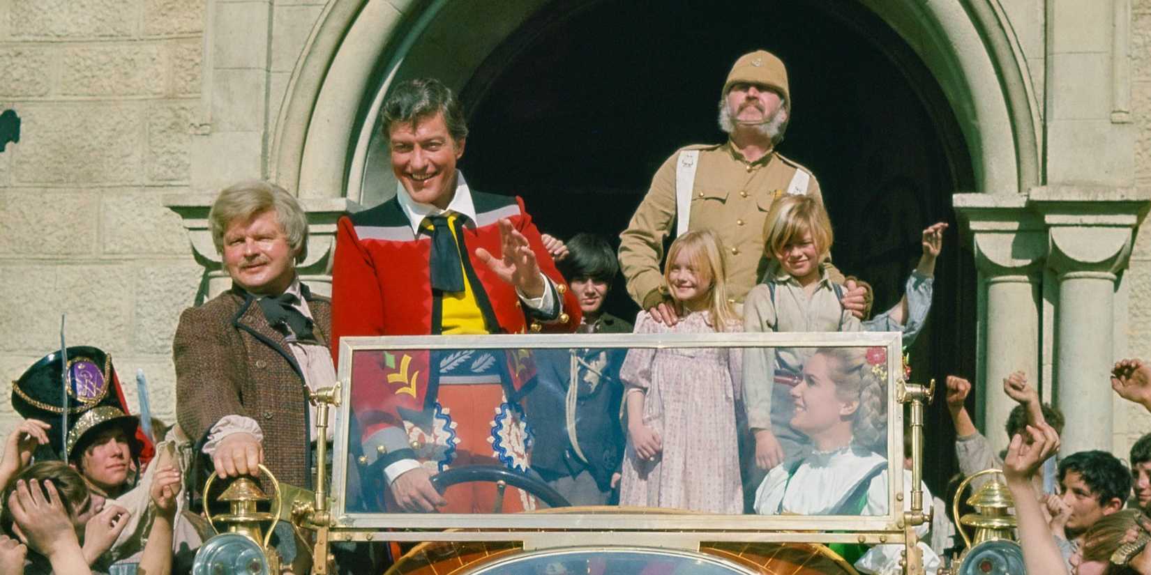 The cast sit in the titular car outside a castle where a crowd of children cheer in Chitty Chitty Bang Bang