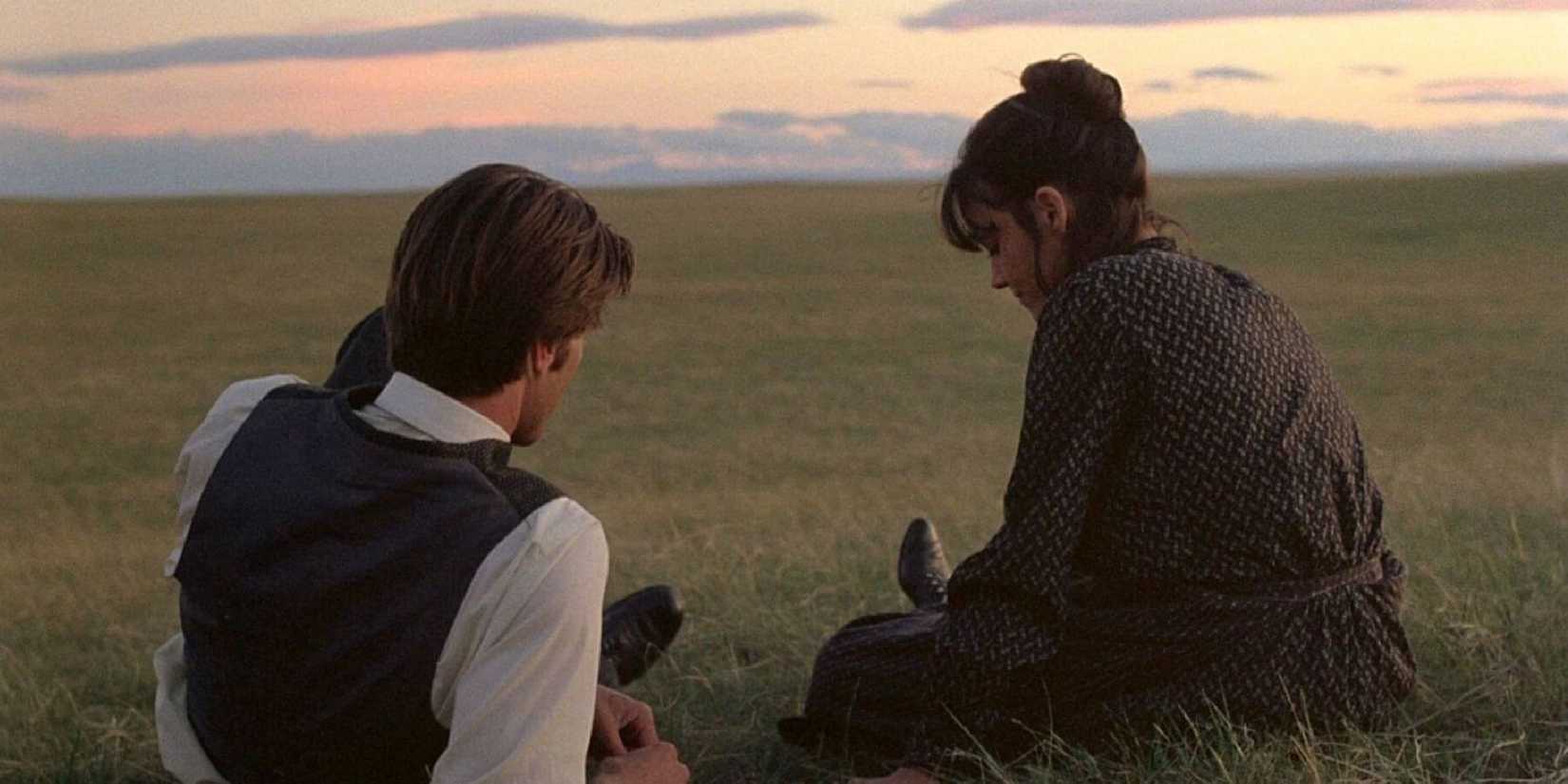 Sam Shepard and Brooke Adams sit side by side on the grass in Days of Heaven