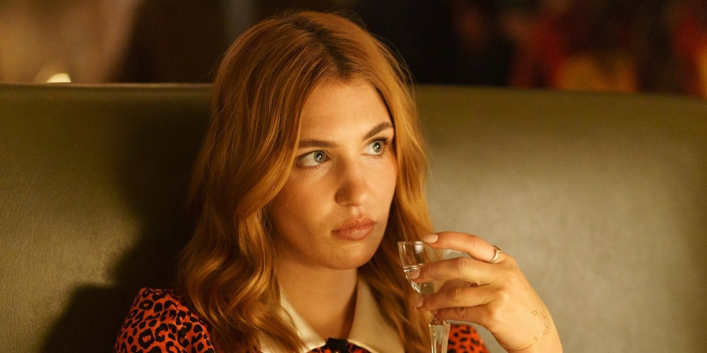 Sophie Nélisse as Rose Landry sitting in a booth at a restaurant while holding a drink in Heated Rivalry