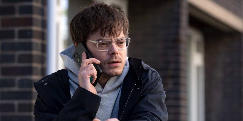 Charlie Heaton as James Dycker leaning on a railing while talking on his cell phone in Industry Season 4