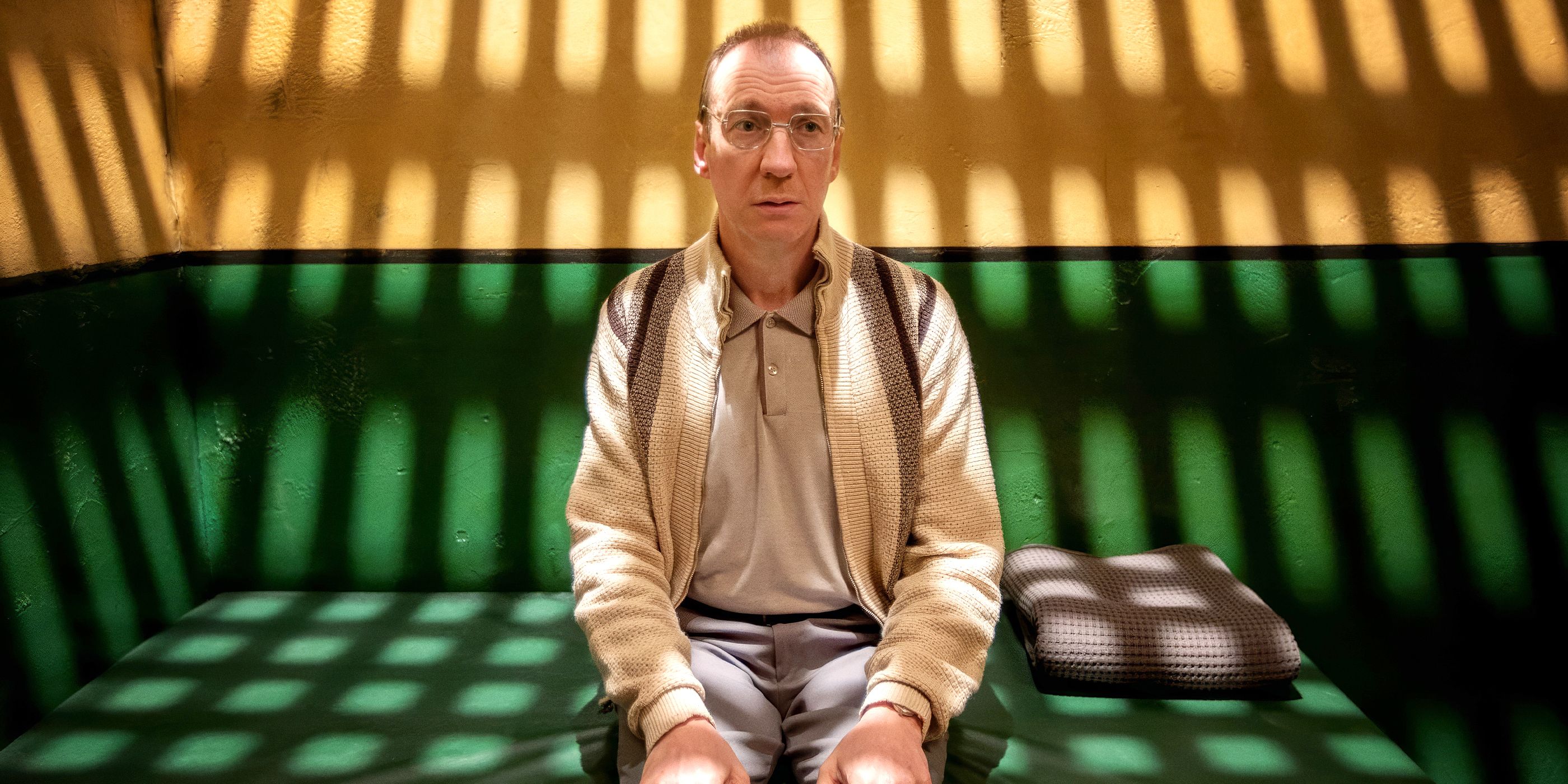 David Thewlis looking off into the distance in a cell with his hands on his lap in Landscapers 