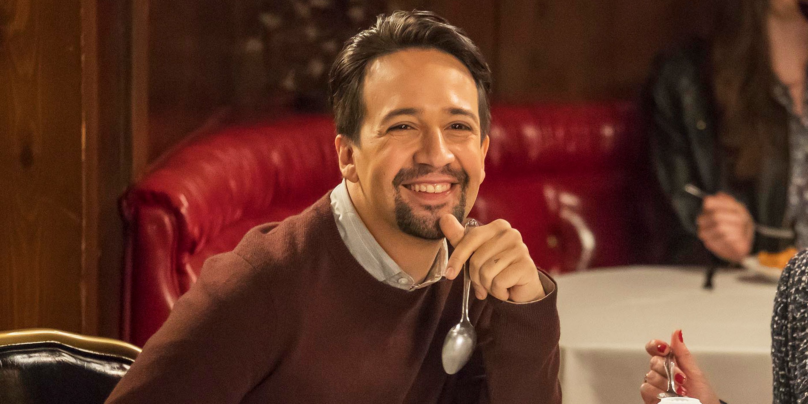 Lin-Manuel Miranda smiling at a table in Brooklyn Nine-Nine