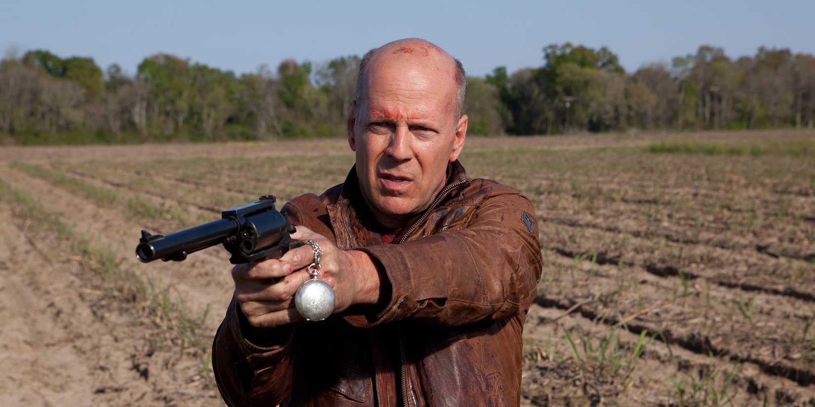 Bruce Willis pointing a gun in a field in Looper