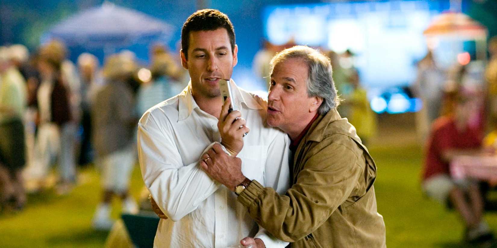 Henry Winkler holding onto Adam Sander at an outdoor event. Sandler holds a remote in Click