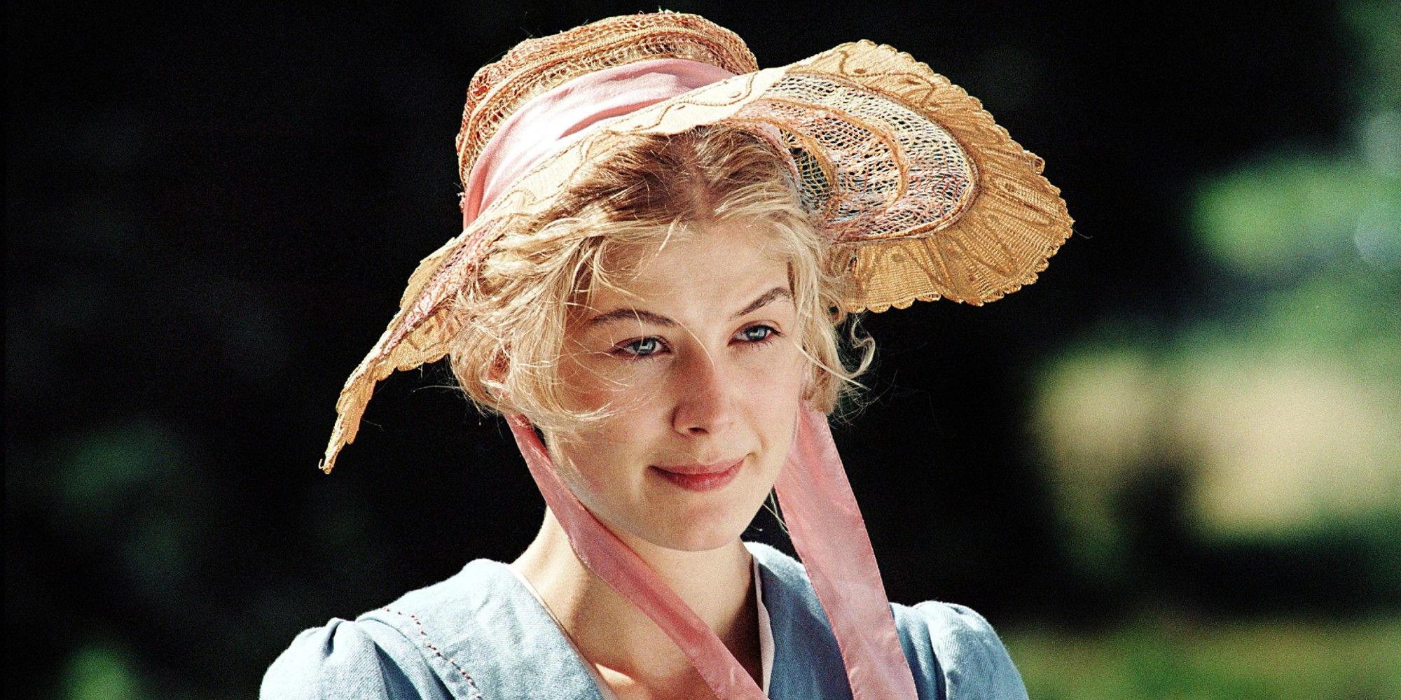 Rosamund Pike standing outside in a sun hat, smiling slightly, in Pride and Prejudice
