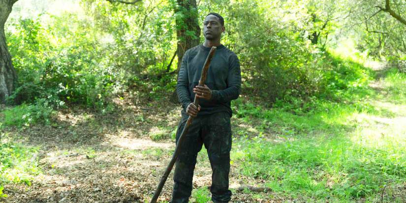 Xavier standing in a forest area during the day and holding a long tree branch in Paradise Season 2 Episode 2