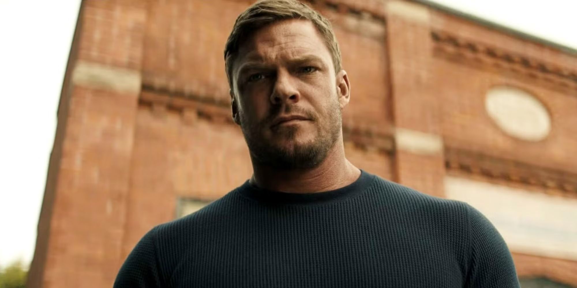 Alan Ritchson looking down at something in Reacher