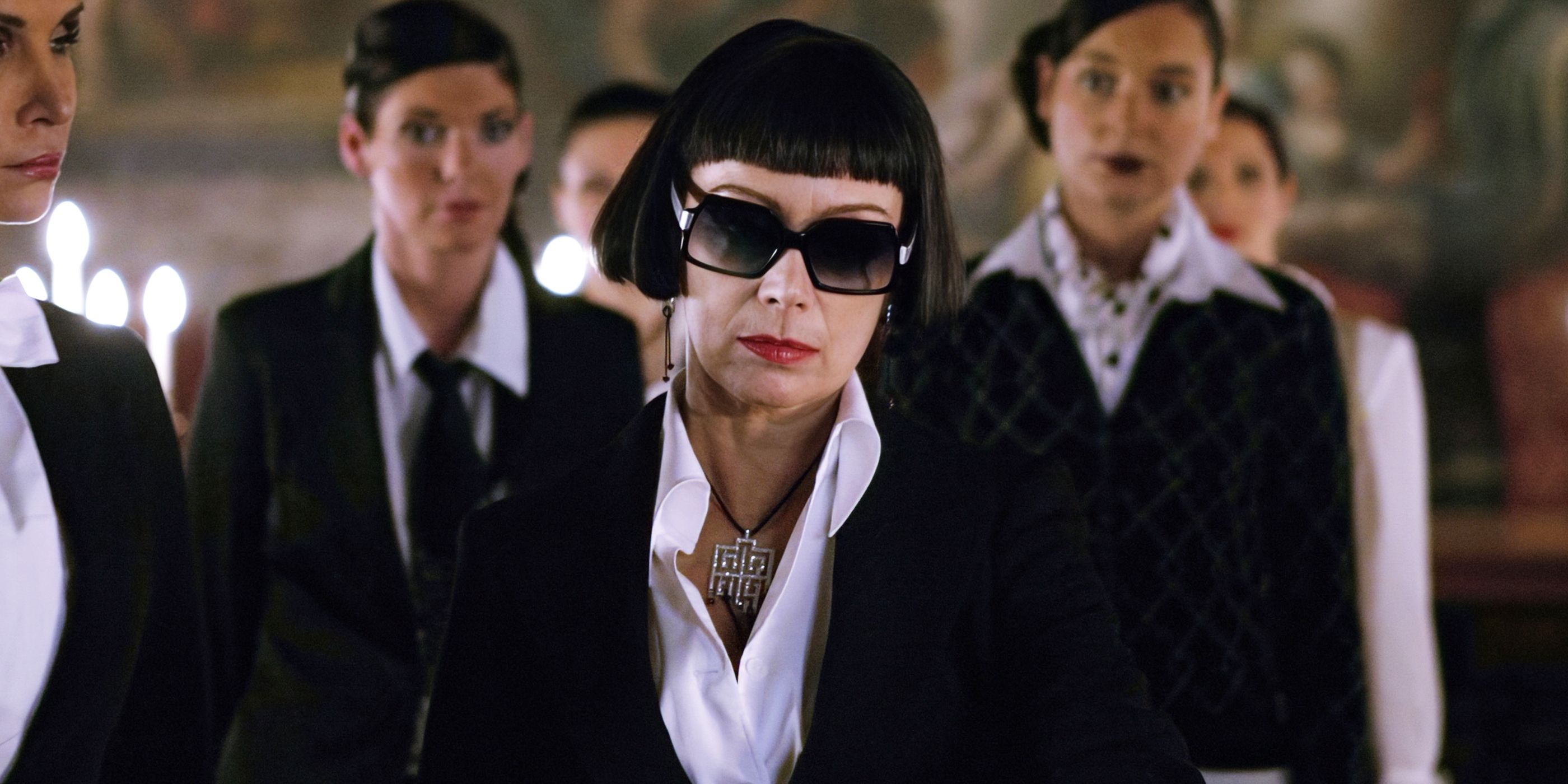 A woman with a sharp black hair cut and big black sunglasses looks off-screen in 'Revolver'