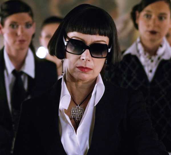 A woman with a sharp black hair cut and big black sunglasses looks off-screen in 'Revolver'