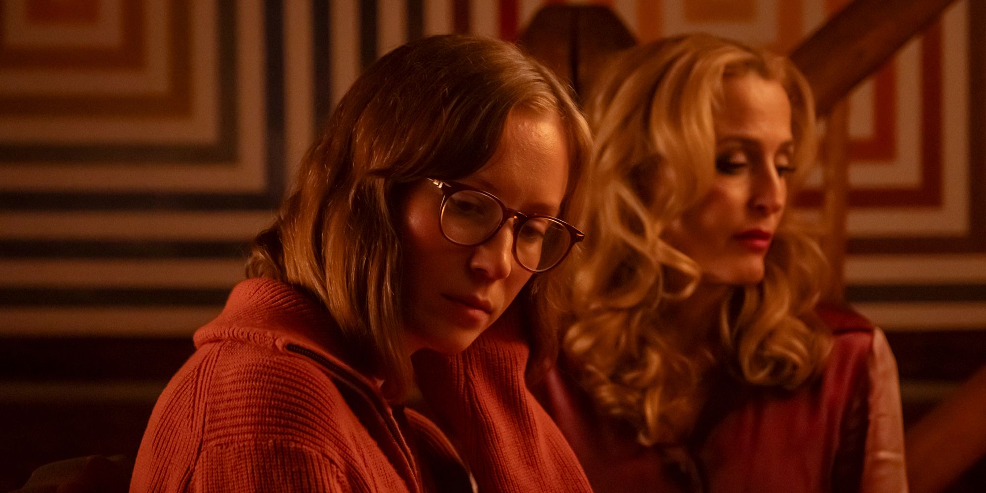 Hannah Einbinder and Gillian Anderson glancing down at something in Teenage Sex and Death at Camp Miasma