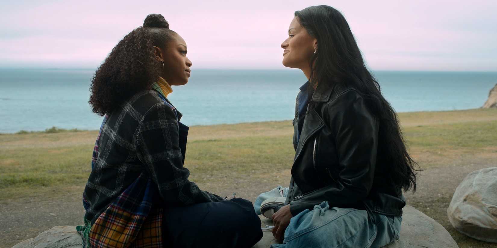 Jazz Raycole as Izzy sitting at the beach on a rock with Gigi Zumbado as Grace in The Lincoln Lawyer Season 4