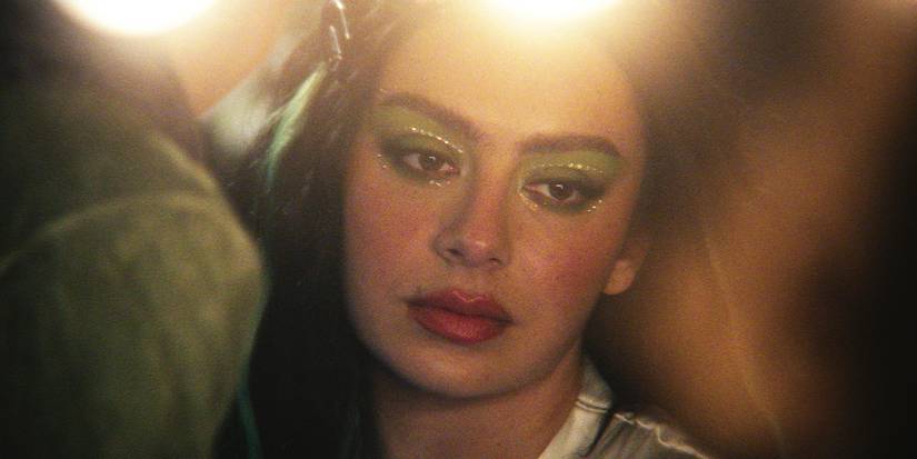 A close-up of Charli xcx looking down, zoning out, with green eyeshadow and rhinestones around her eyes.
