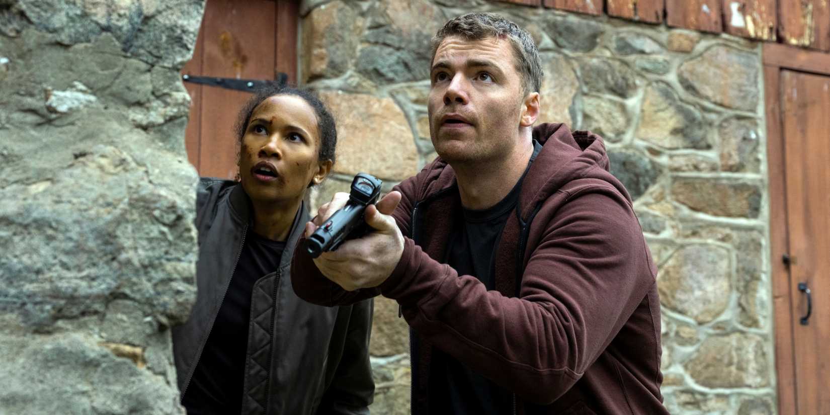 Gabriel Basso as Peter Sutherland holding a gun next to Fola Evans-Akingbola as Chelsea in The Night Agent