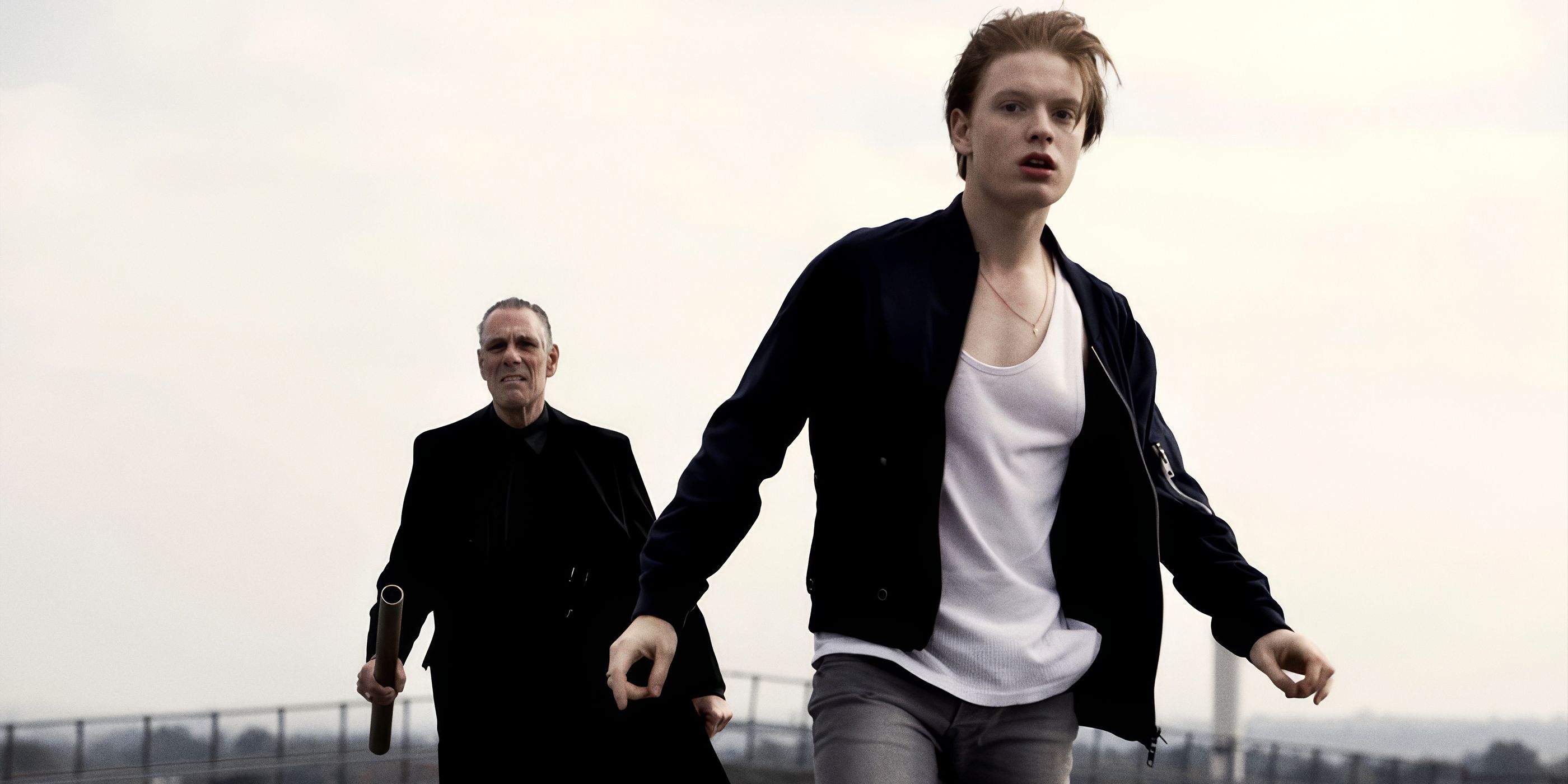 Freddie Fox walking with his hands out away from a man with a gun in The Shadow Line