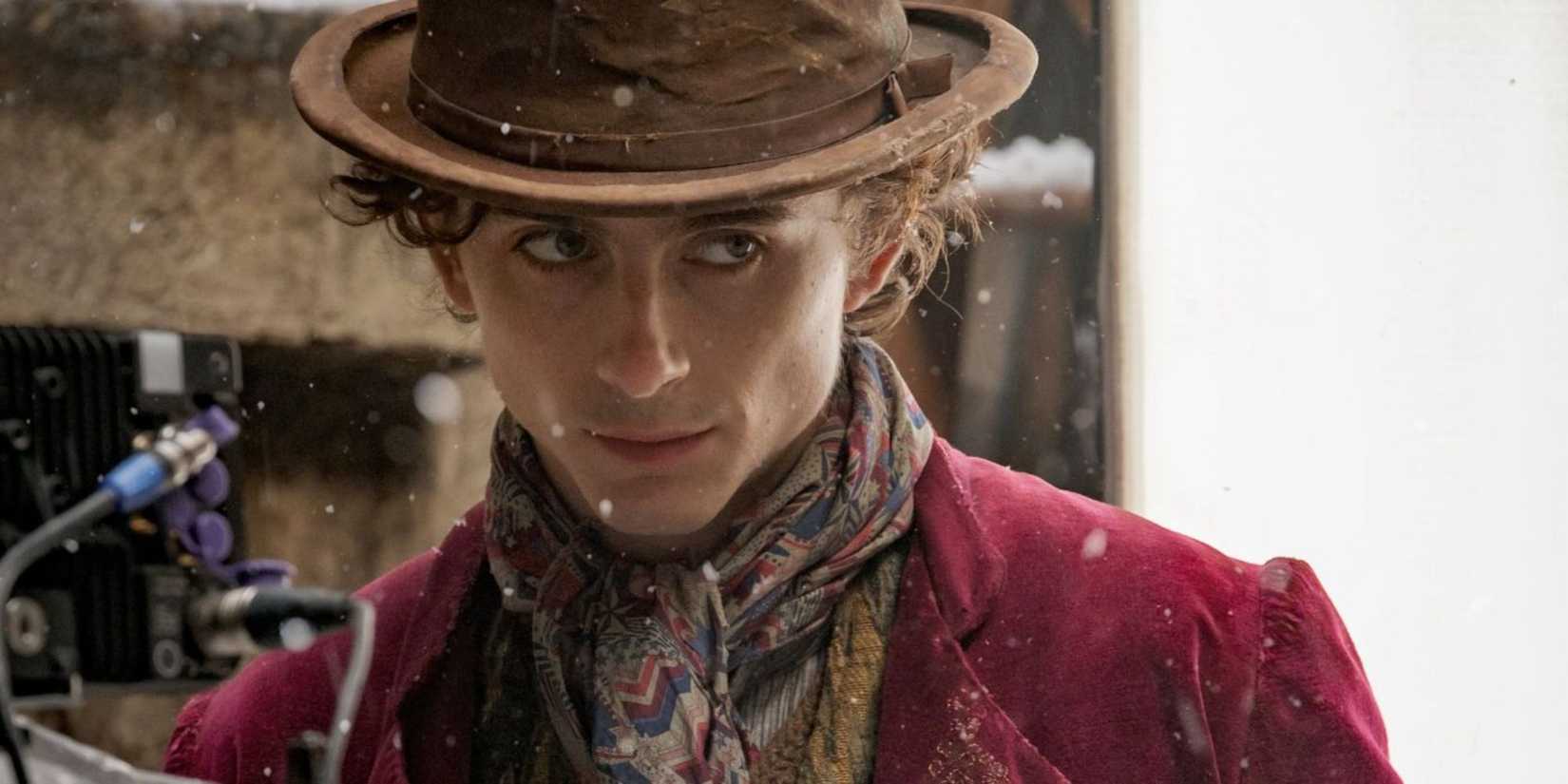 Timothée Chalamet as Willy Wonka in a top hat looking to the side intently with snow falls in Wonka