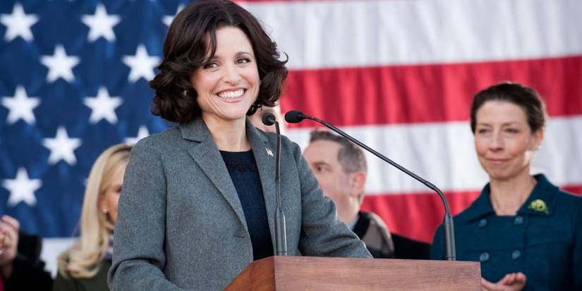 Julia Louis Drefyus as Selina Meyer standing at a podium with an American flag behind her in Veep.