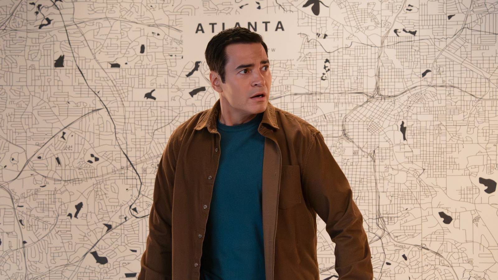 Ramón Rodríguez as Will Trent standing in front of a map and looking upset in Will Trent Season 4 Episode 7