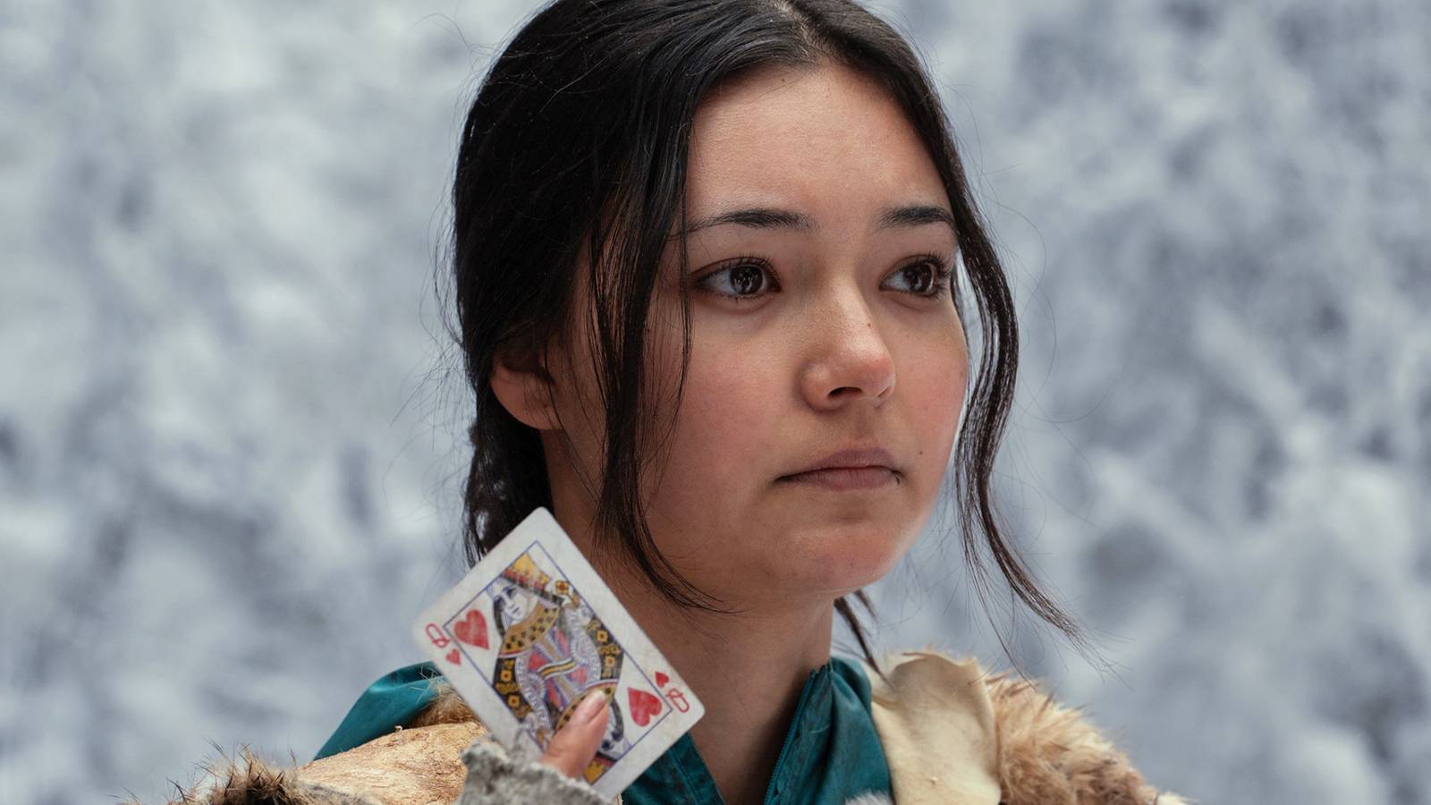 a woman in Yellowjackets holds up a queen of hearts card