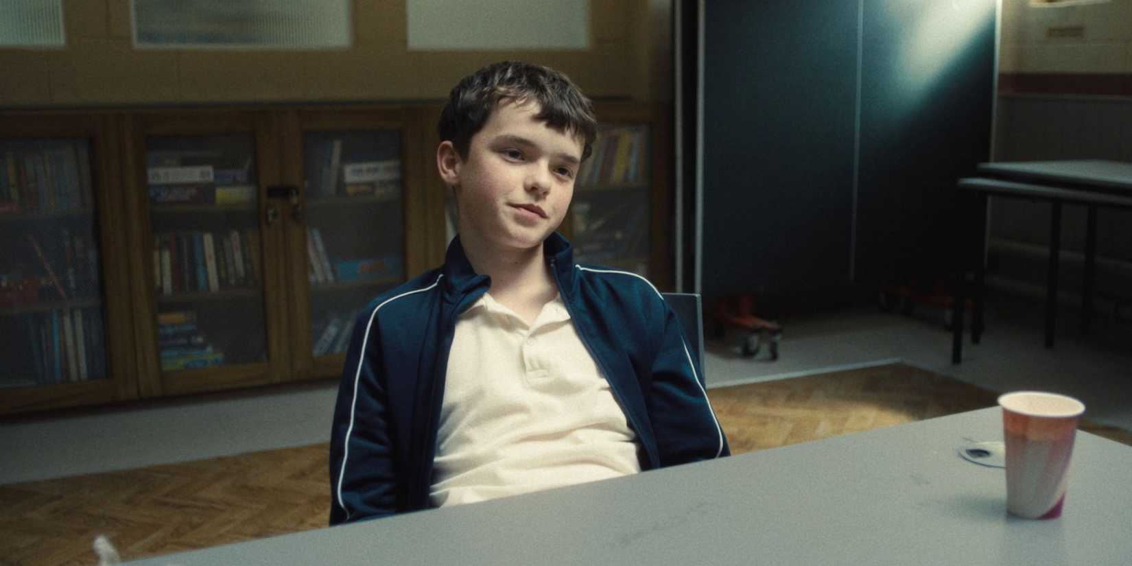 Jamie smirking while sitting at a table in Adolescence